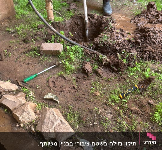 A person digging near plumbing pipes with tools on the ground.